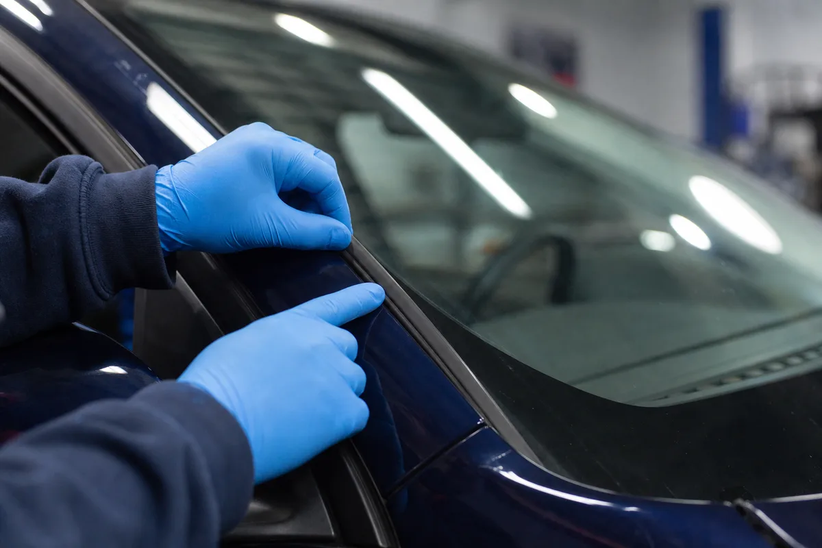 Mécanicien en atelier examinant un pare-brise de voiture citadine, plan rapproché sur les mains et le vitrage