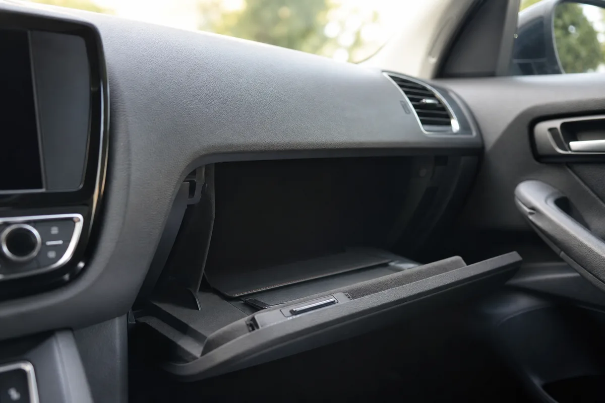 Automobiliste rangeant des documents administratifs dans la boîte à gants d&rsquo;une voiture, mains seules visibles, intérieur de véhicule